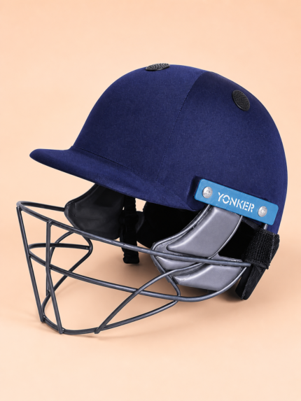 Navy YONKER cricket helmet front three-quarter view on pastel apricot background